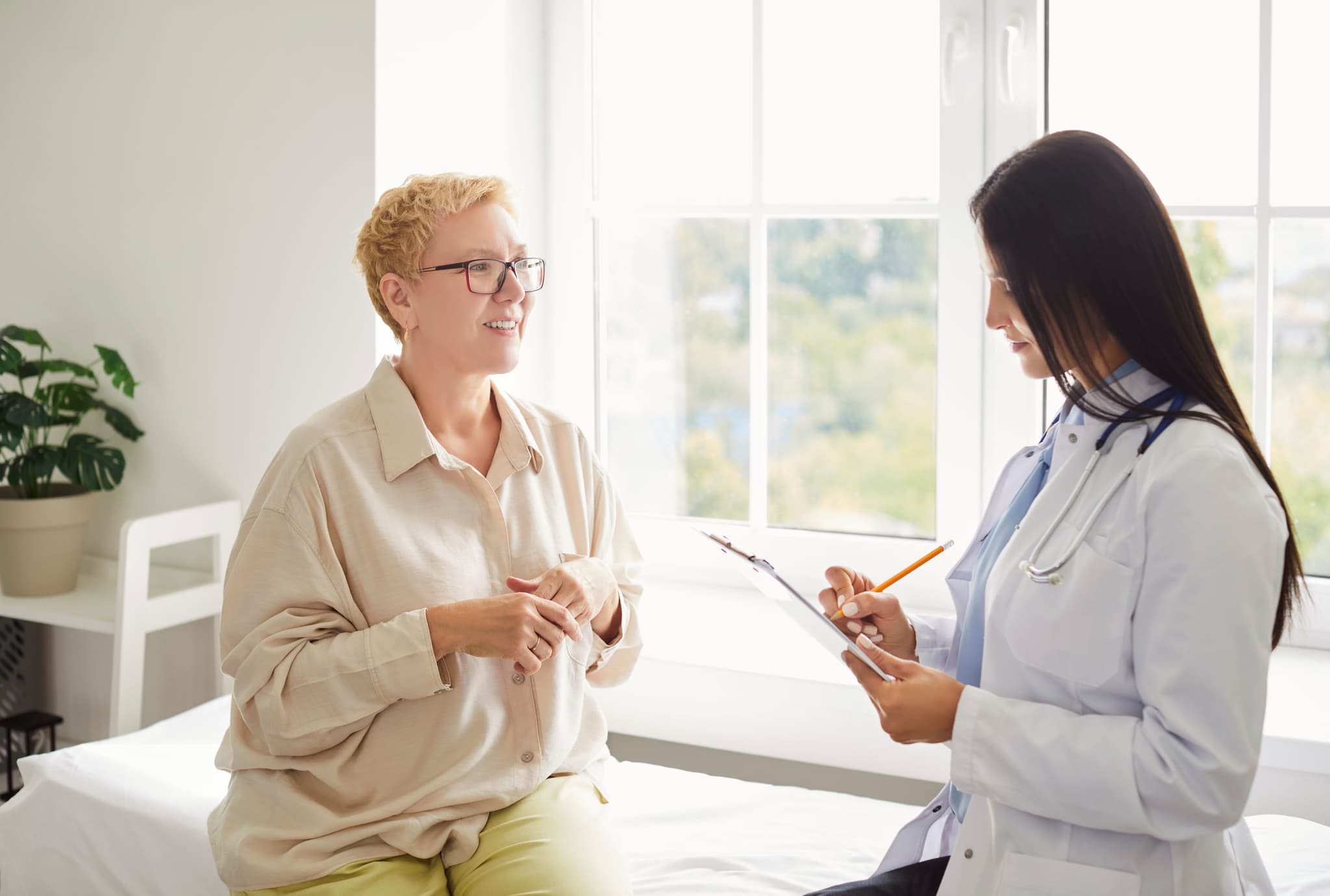 A nephrologist performing a thoughtful patient exam in a sunlit consultation room